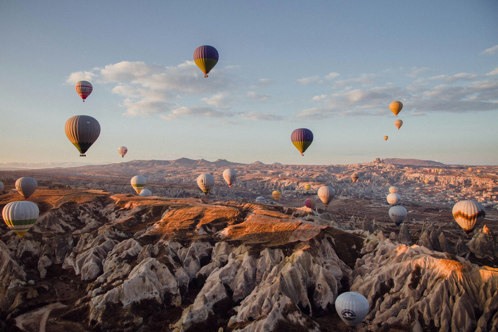 A wide Cappadocia valley at sunrise with scattered balloons